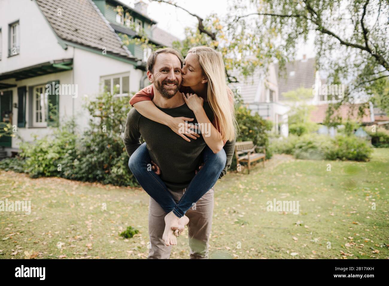 Woman kissing man, carrying her piggyback in garden Stock Photo