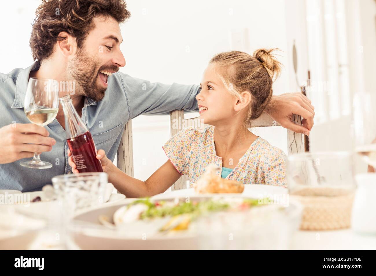 Father and daughter sitting at dining table toasting Stock Photo