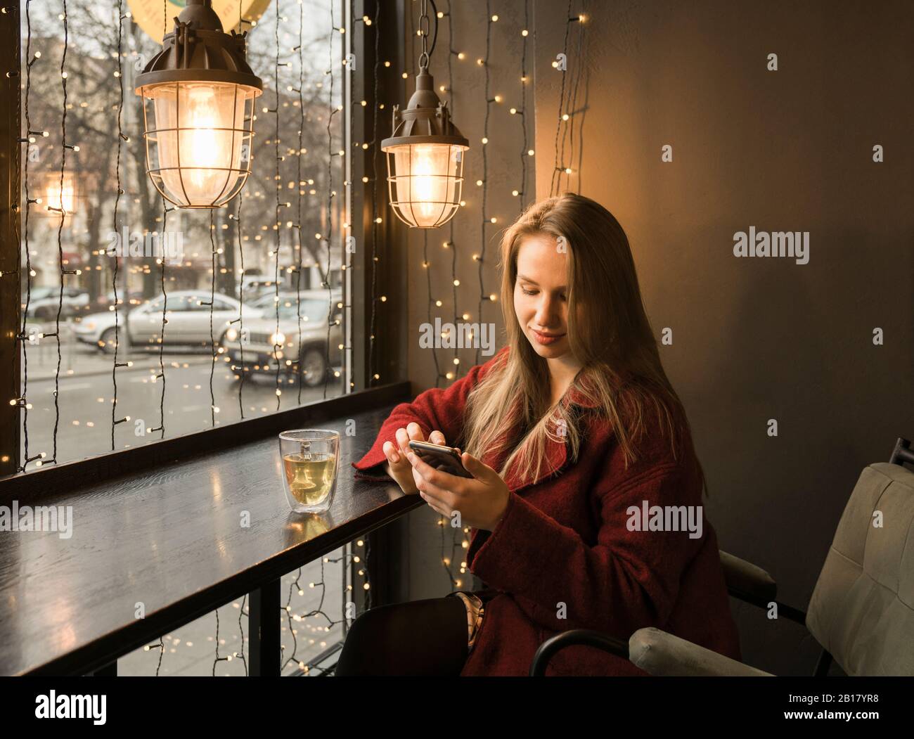 Young woman with cup of tea sitting in a coffee shop using mobile phone Stock Photo