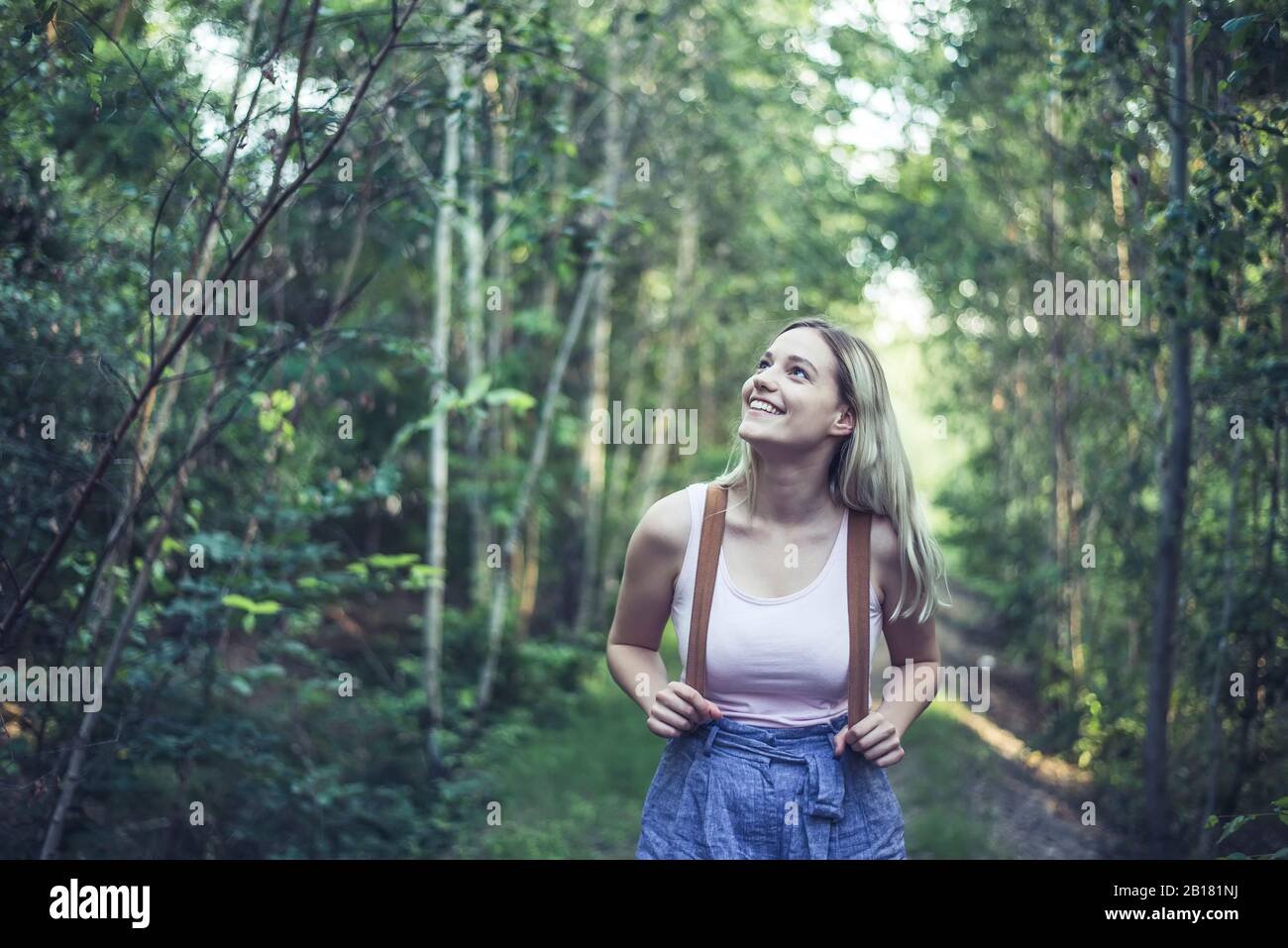 Portrait of smiling young woman with backpack in forest watching something Stock Photo