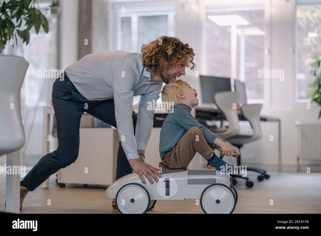 Businessman pushing son on toy car in office Stock Photo