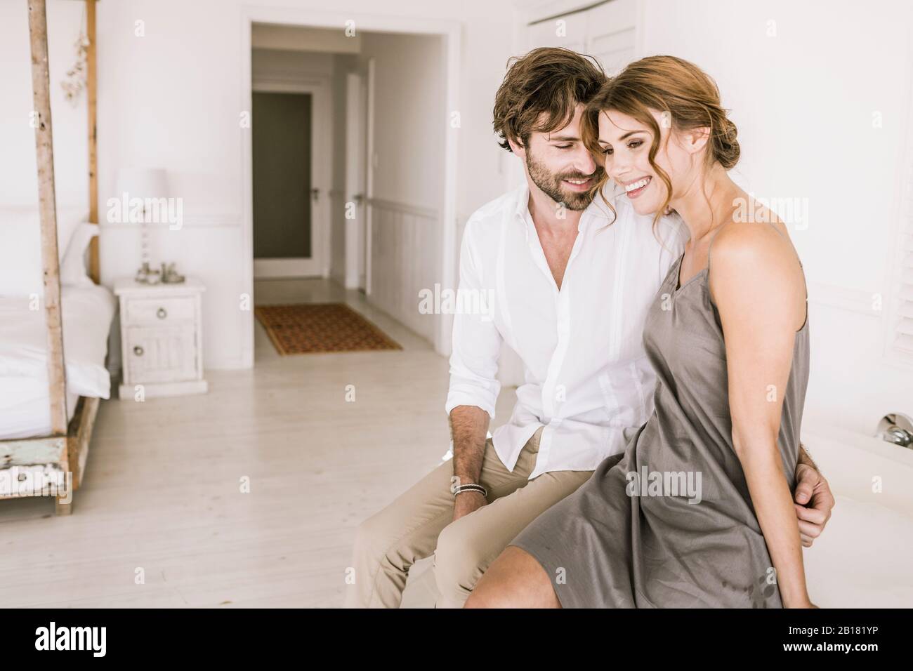 Happy young couple sitting in bedroom Stock Photo