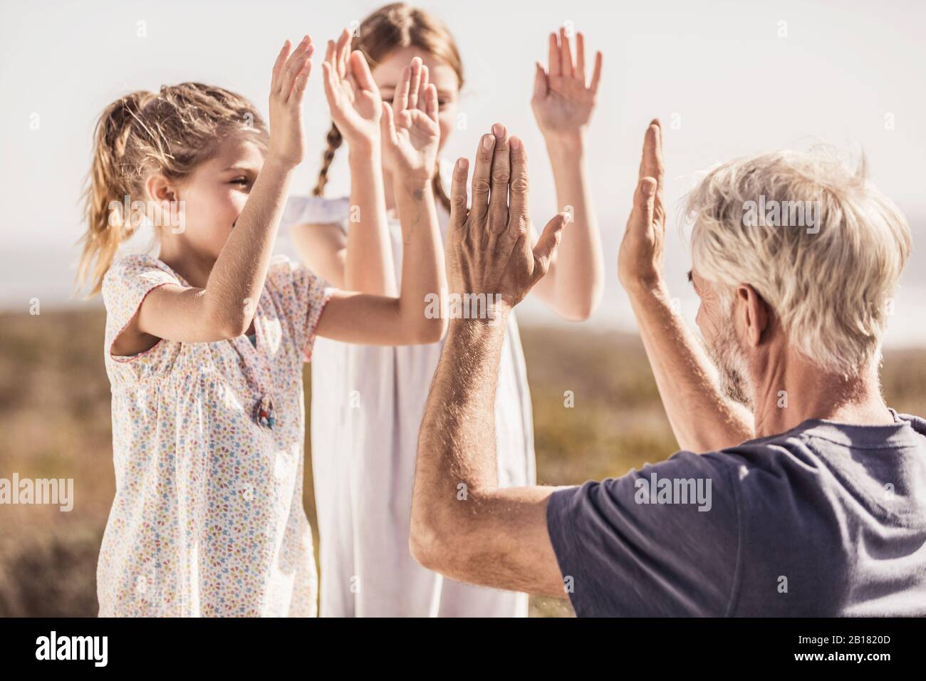 Two girls clapping hands with their grandfather Stock Photo
