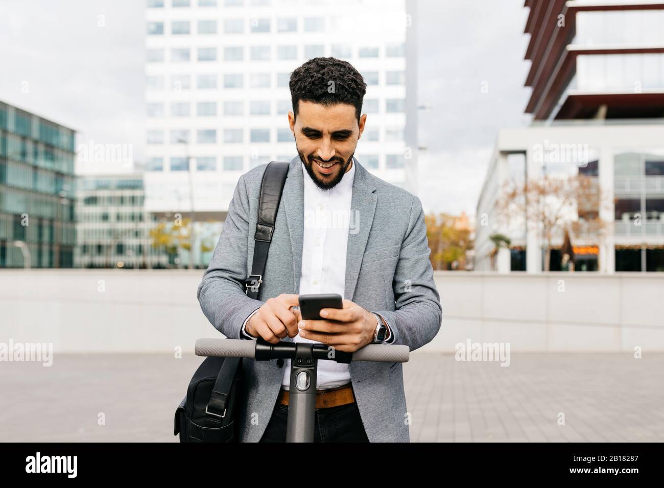 Casual young businessman with electric scooter using cell phone in the city Stock Photo