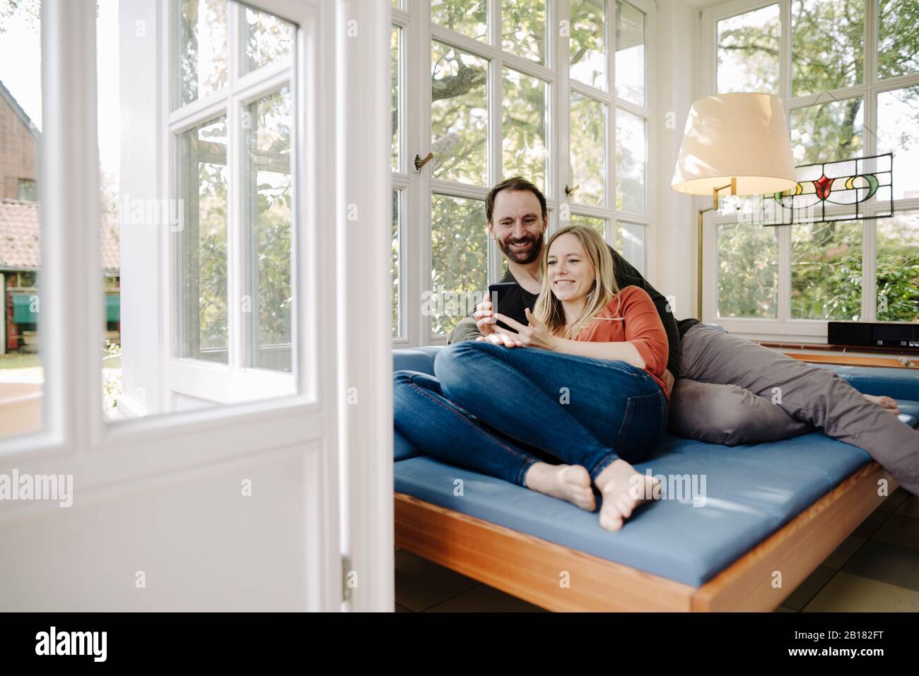 Happy couple relaxing on couch, using smartphone Stock Photo