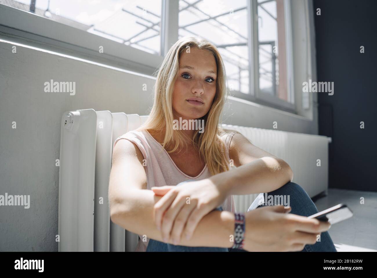 Portrait of blond young woman sitting on the floor Stock Photo - Alamy