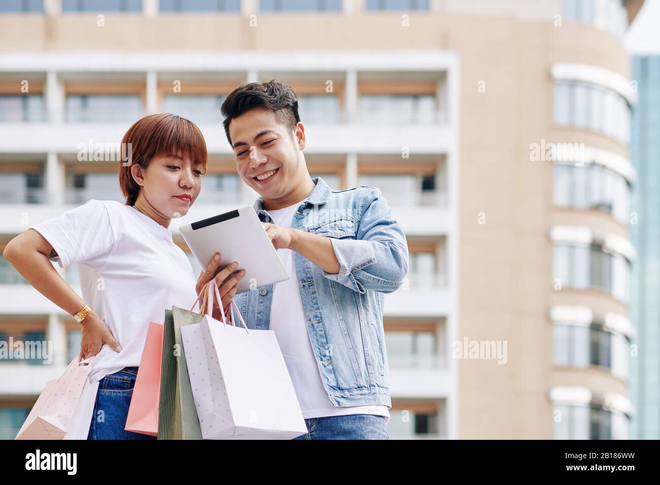 Happy young Vietnamese couple using application on tablet computer when shopping online Stock Photo