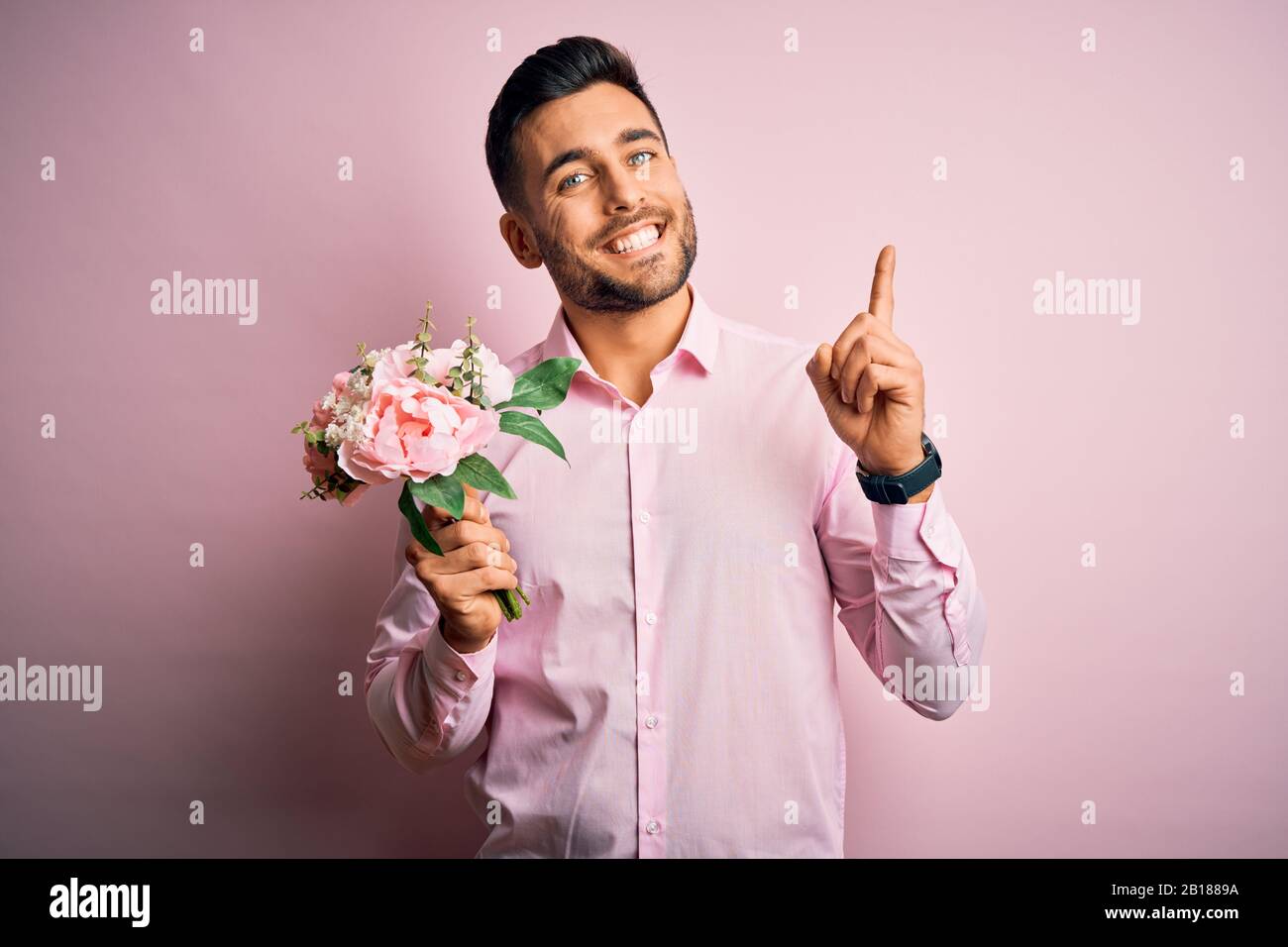 Young romatic man holding bouquet of spring flowers over pink isolatd ...