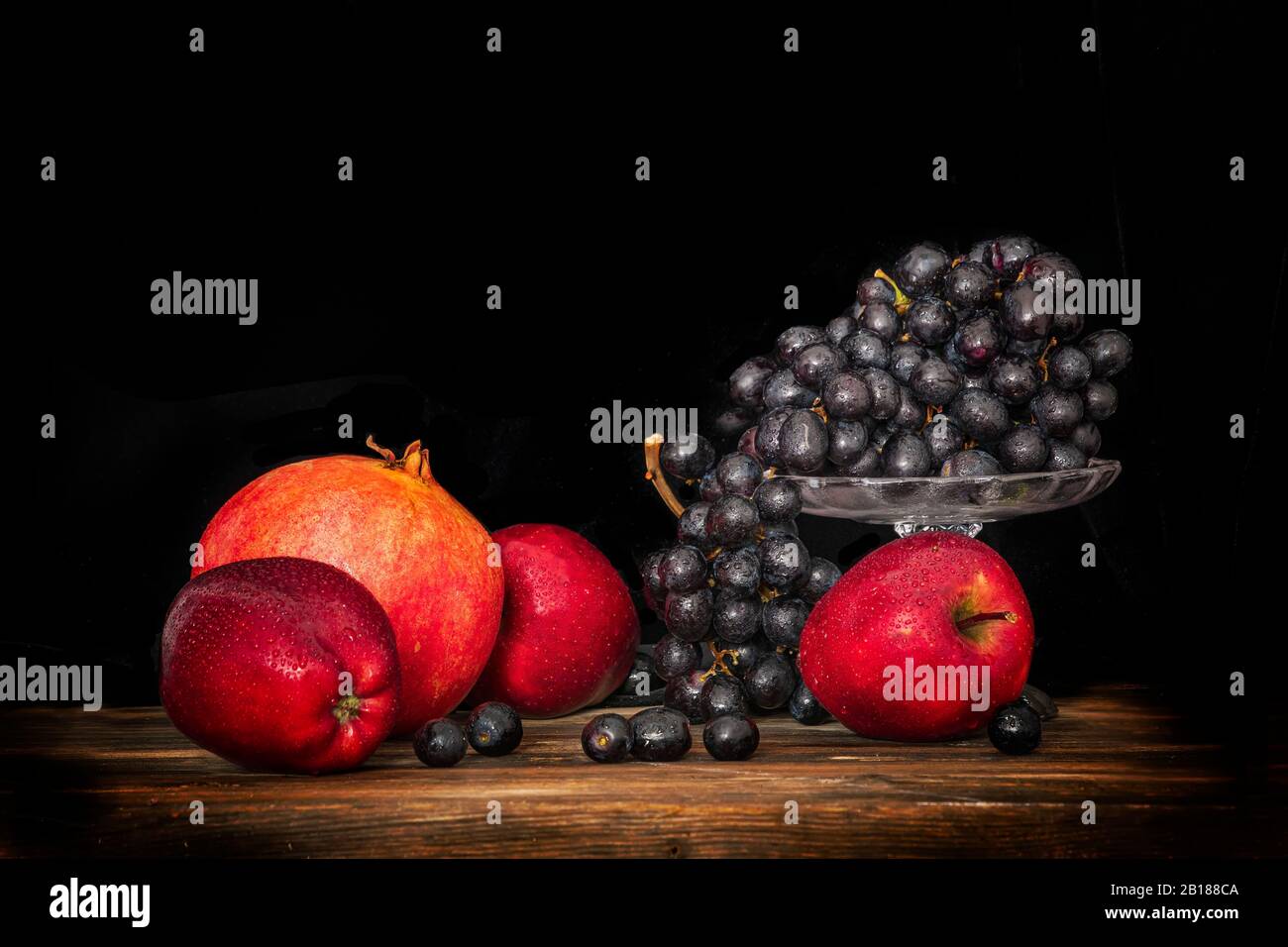 Still life apples, black grapes and pomegranate on a wooden surface and on a black background Stock Photo