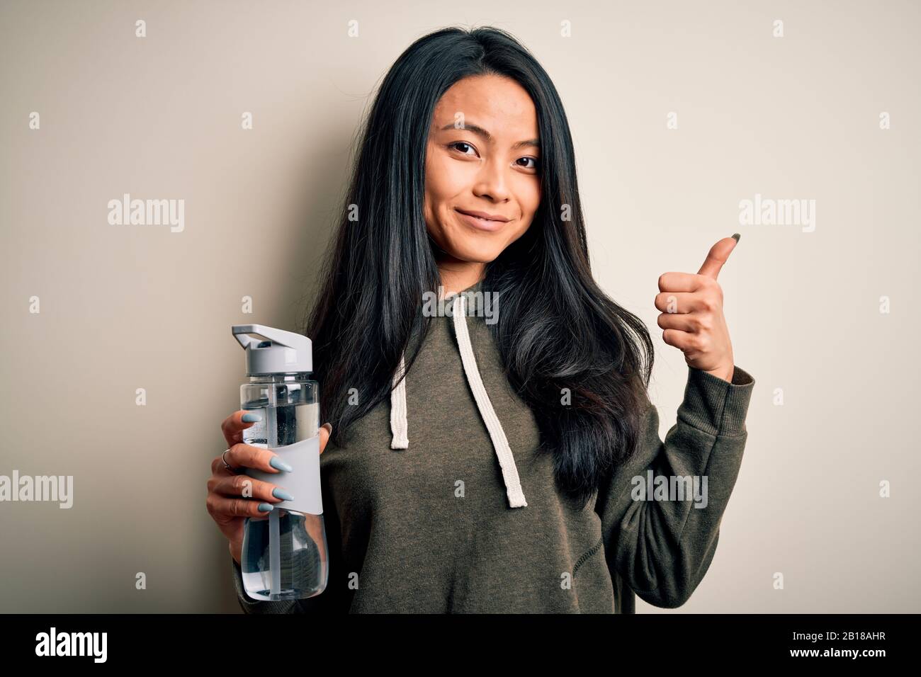 Young beautiful chinese sportswoman holding bottle of water over ...