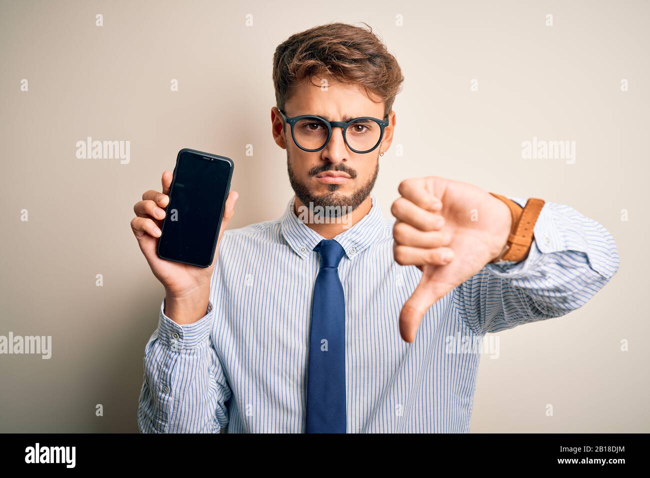 Young businessman holding smartphone standing over isolated white ...