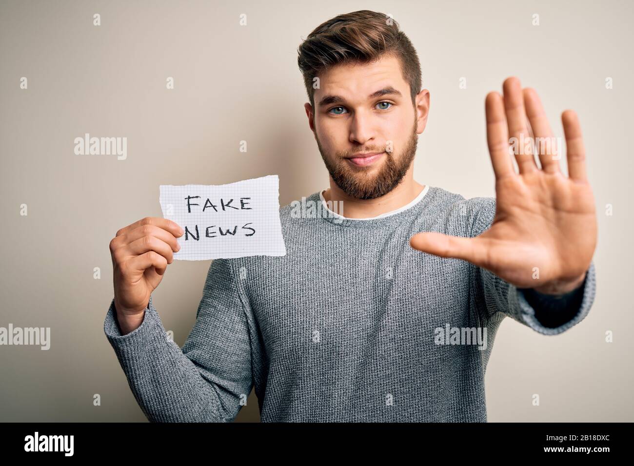 Young blond man with beard and blue eyes holding paper with fake news ...