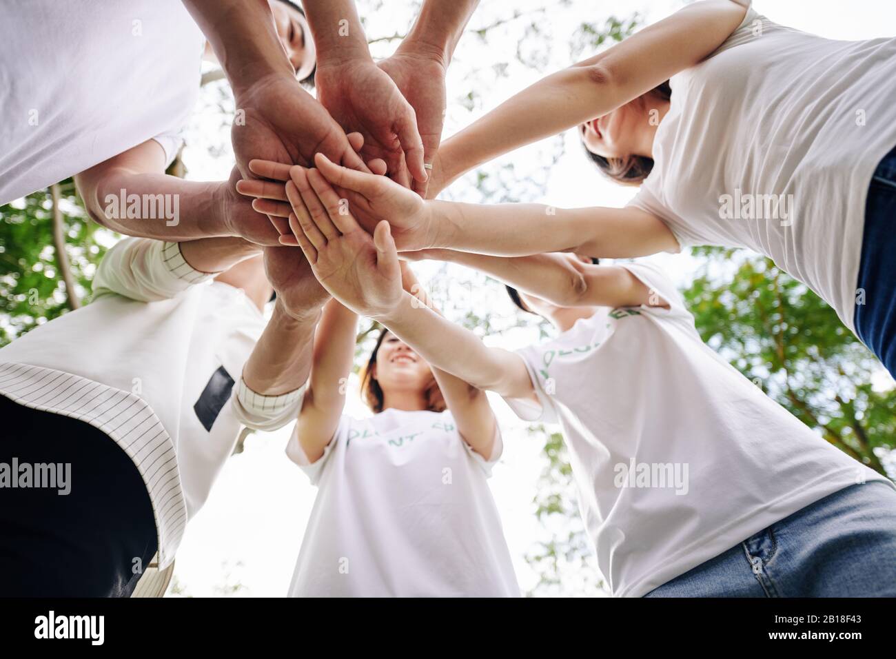 Team of student volunteers stacking hands to show support and unity before starting cleaning college campus Stock Photo