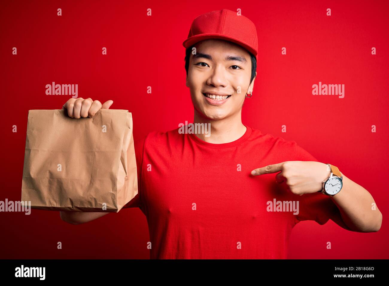 Young handsome chinese delivery man holding takeaway paper bag with