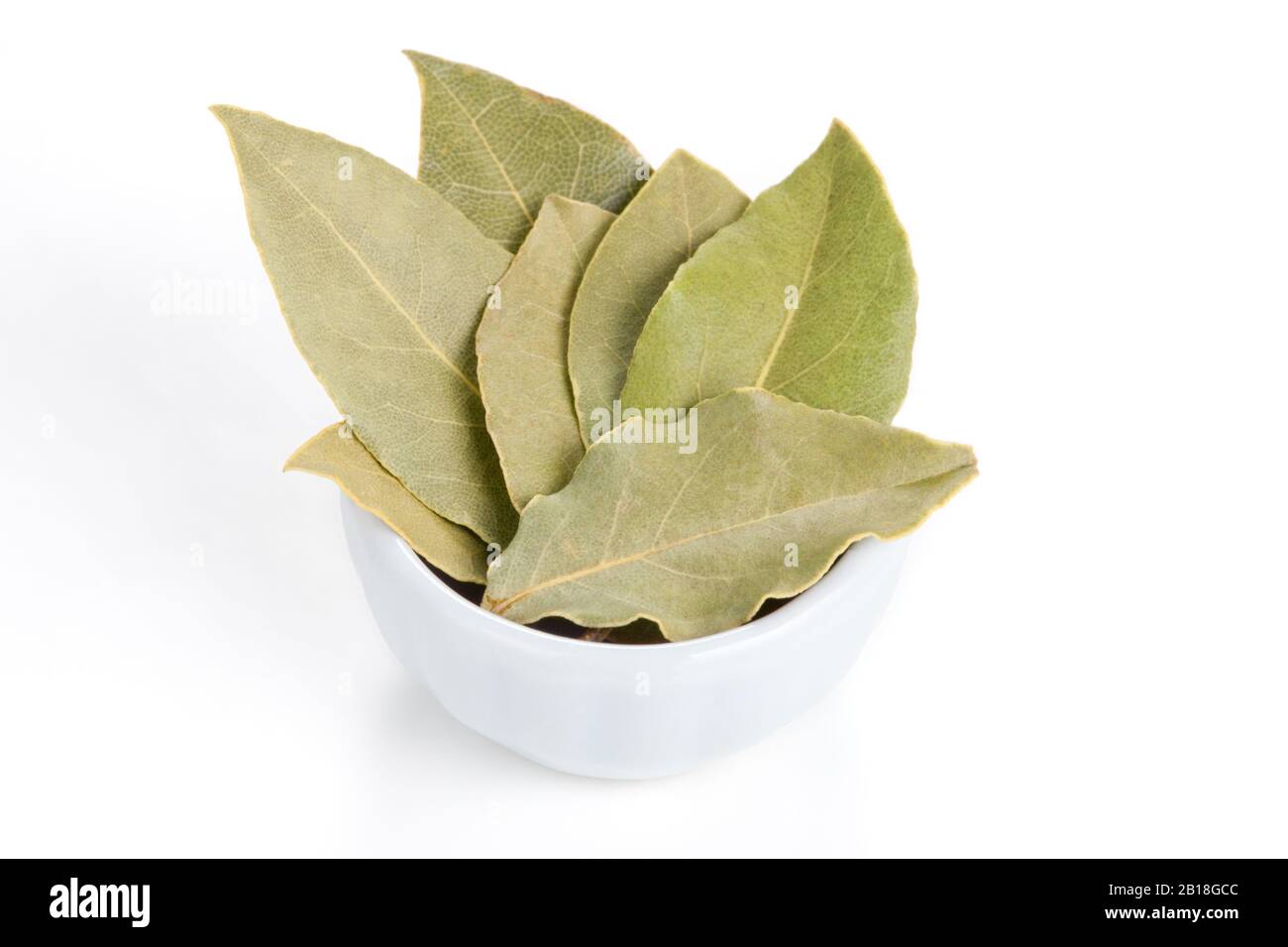 Bay Leaves in a white bowl on white background. Also called bay laurel or Laurus nobilis. Used as a spice in cuisines and also in medicine. Stock Photo