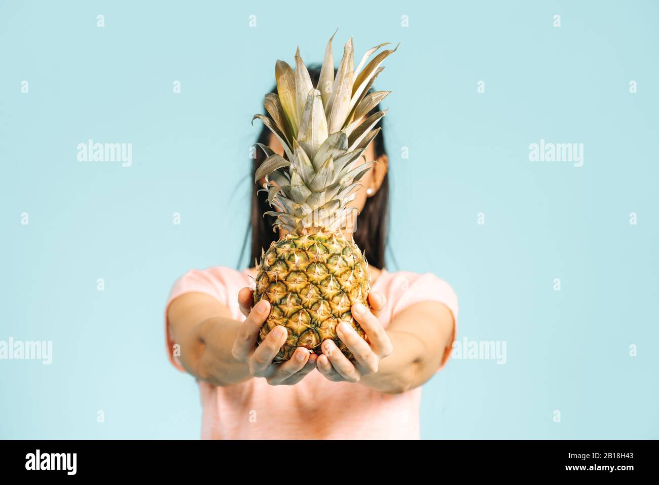 Young woman is holding a fresh and delicious pineapple and posing isn studio front of a blue font isolated Stock Photo