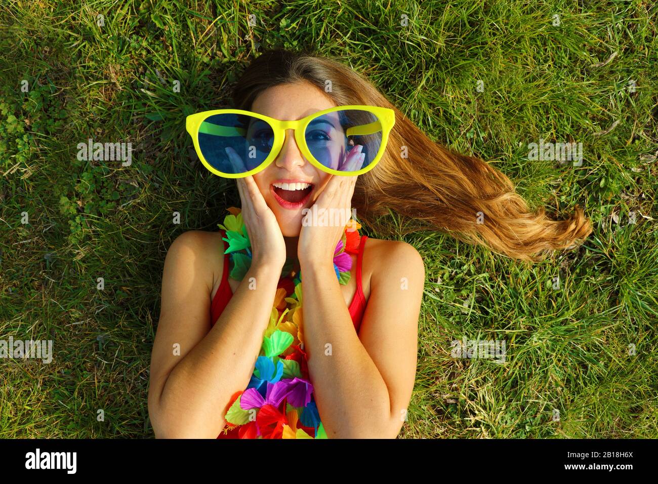 Surprised girl wake up on grass after Carnival party. Happy excited oung  woman with carnival garland and big funny sunglasses lying on grass Stock  Photo - Alamy