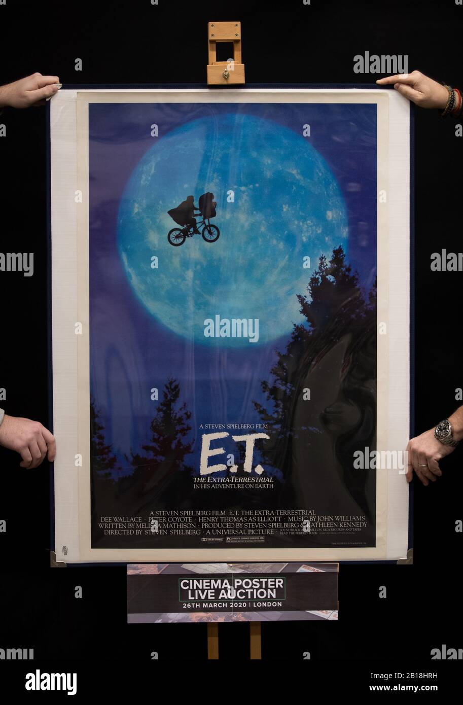 Prop Store employees hold a US One-Sheet Poster for the 1982 film 'E.T, The Extra Terrestrial' (estimate £800 - £1,200), during a preview for the Prop Store's forthcoming cinema poster auction. Stock Photo