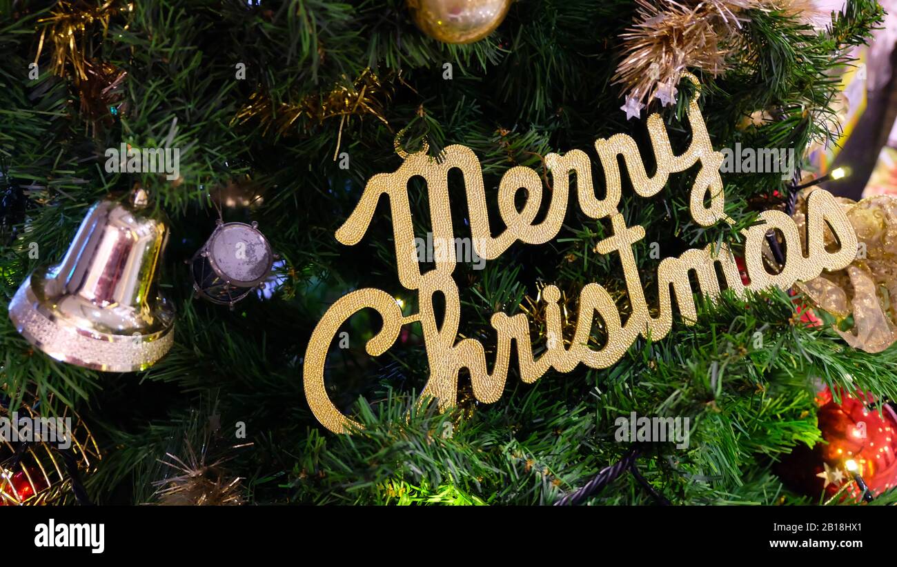 Closeup of a Christmas tree decorated with a gold wording of 'Merry Christmas', silver bell and other ornaments. Stock Photo