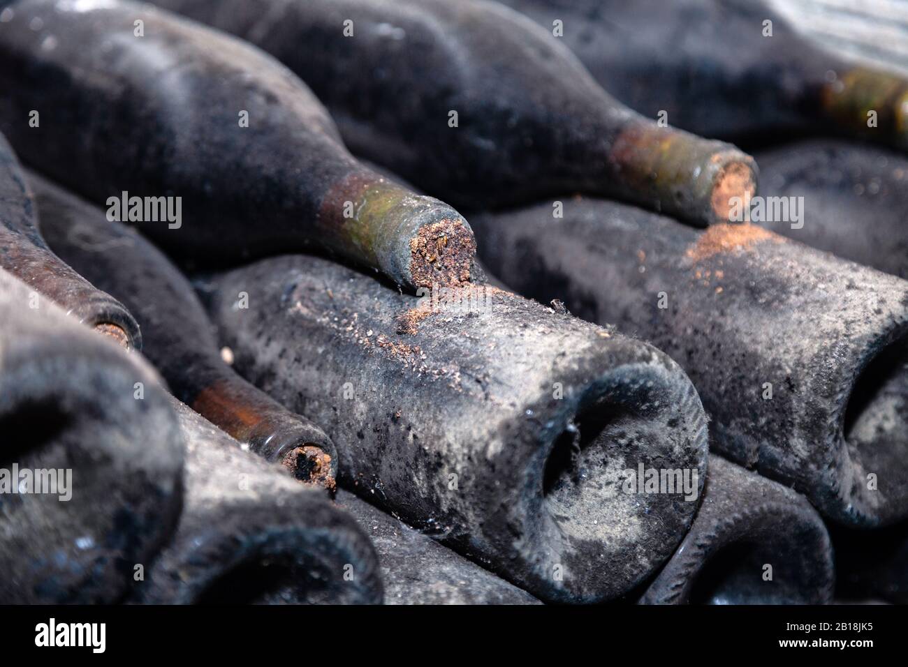 Closeup dark dusty wine bottles with old crumbly cork. Long aging, musty winery vault, rare