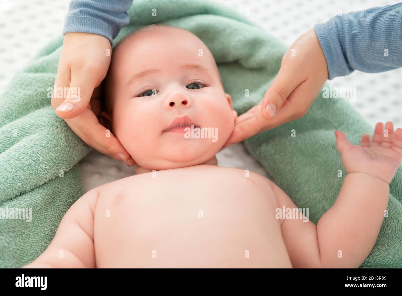 Baby face massage. Mother gently stroking baby boy face with both hands. Close up cropped shot. Stock Photo