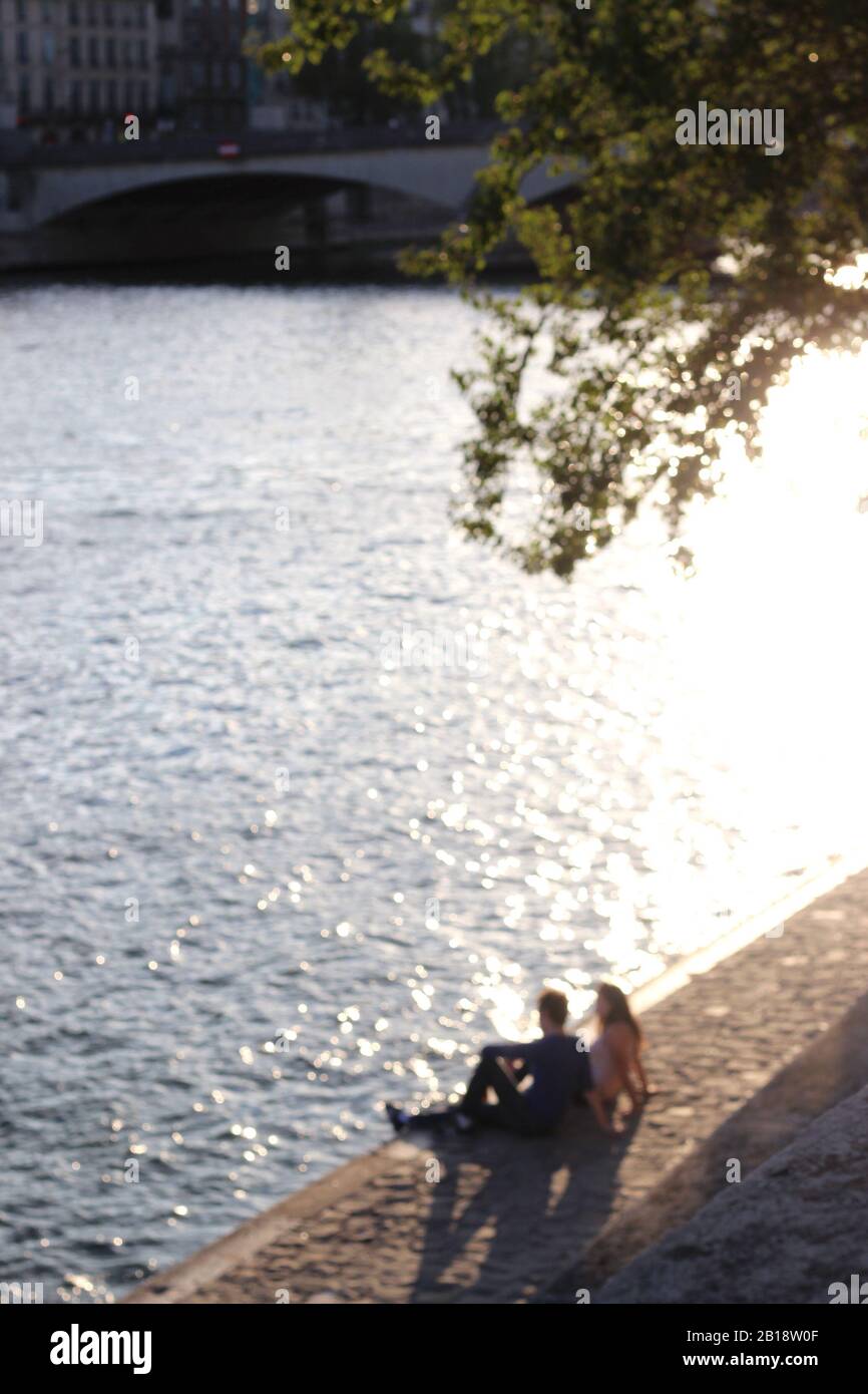 Paris, France. Couple in Love Sitting along the Seine. Blurred Romantic Parisian Life Scene. Stock Photo