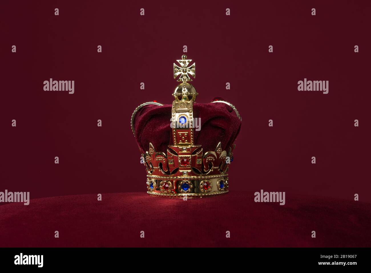 Golden crown on a velvet cushion on a deep red background with copy ...