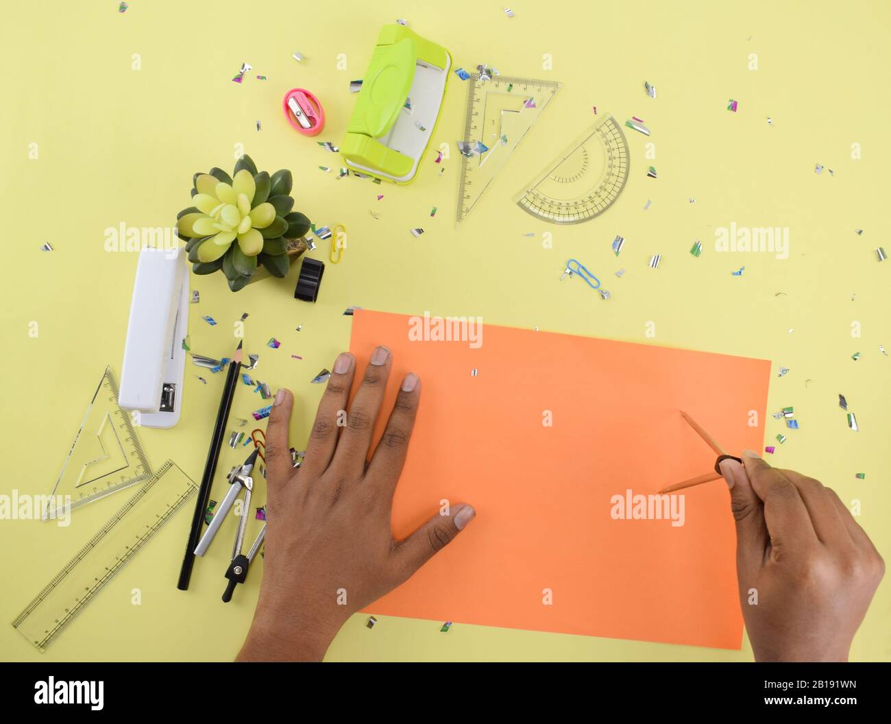 https://c8.alamy.com/comp/2B191WN/various-study-materials-scattered-on-a-yellow-paper-background-while-a-person-is-drawing-on-a-orange-paper-with-a-compass-2B191WN.jpg
