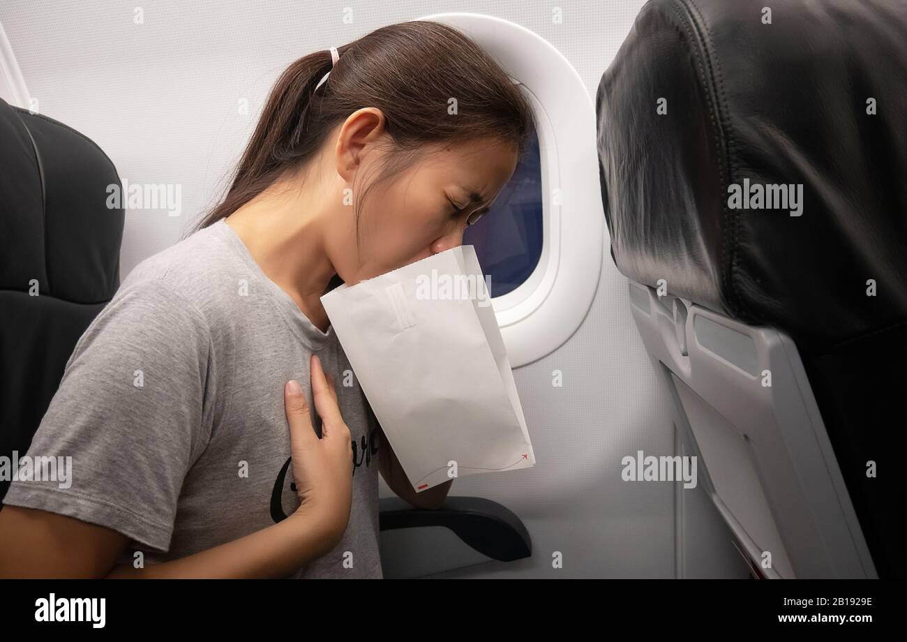female passenger on the plane felt airsick, affected with nausea due to travel in an aircraft using air sickness bag for vomiting due to airsickness Stock Photo