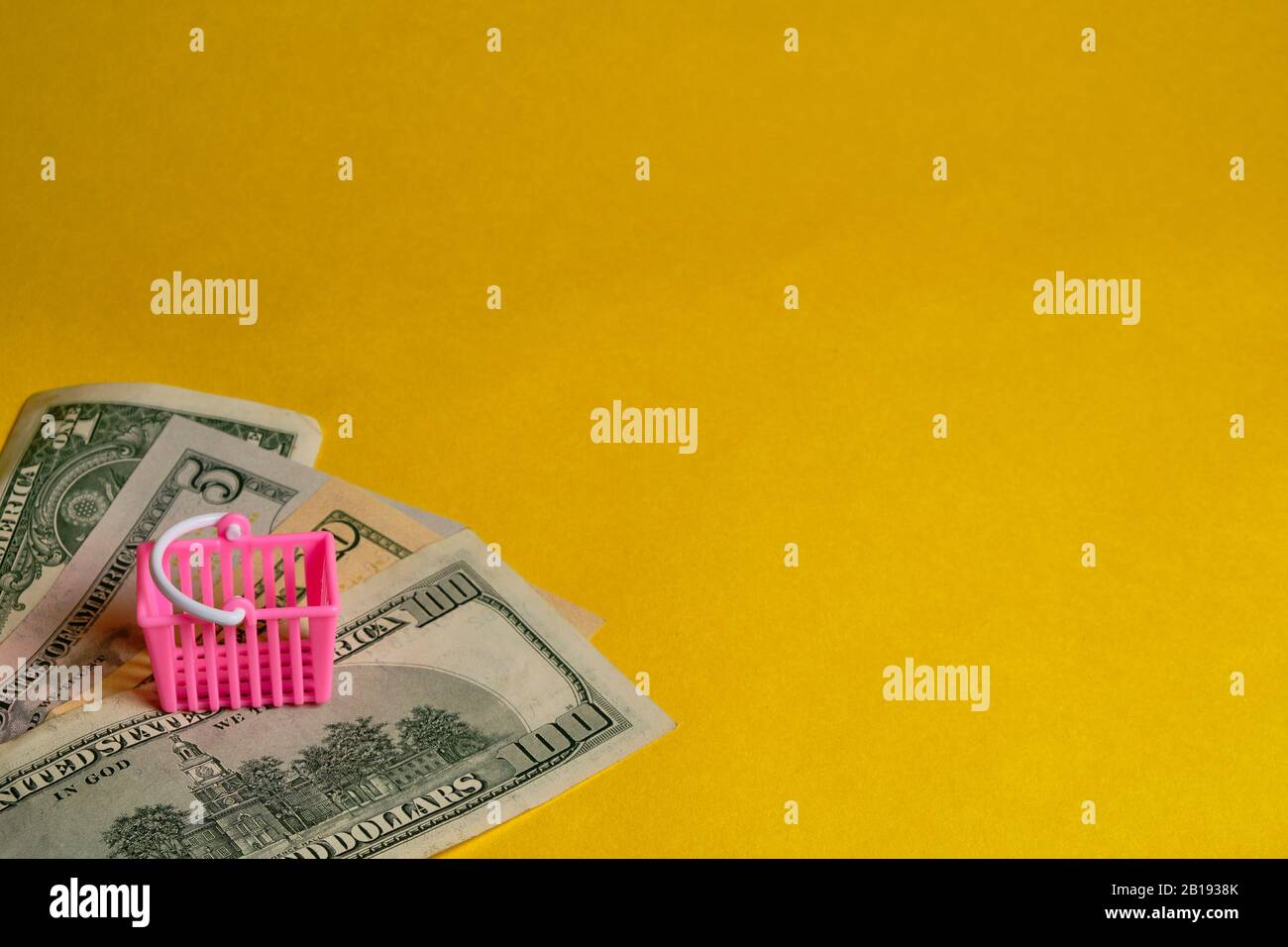 Pink shopping basket and dollar banknotes at yellow background. Shopping, personal finances, money savings concept. Stock Photo