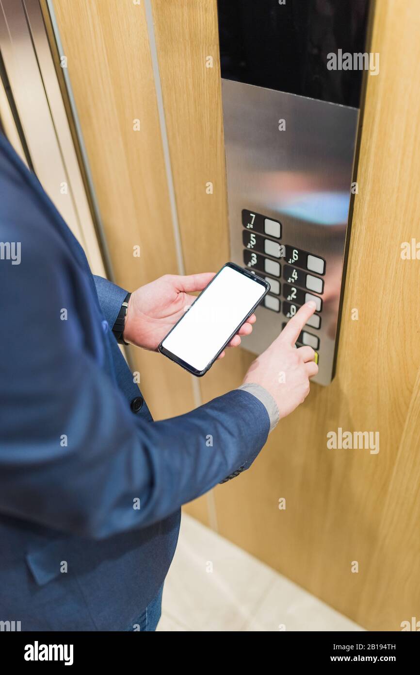 Man hands holding blank screen mobile phone while using elevator control panel. Stock Photo