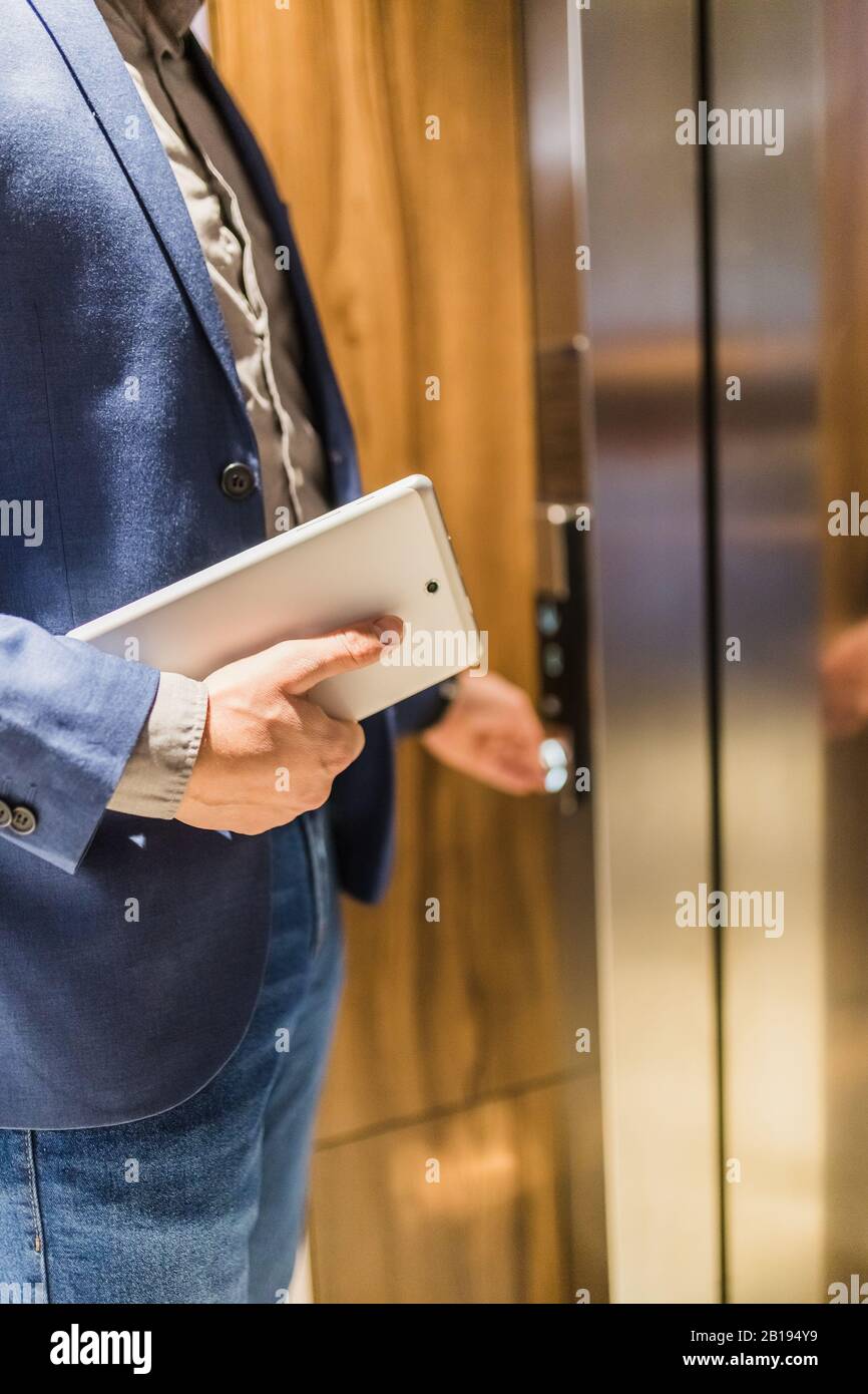 Man holding digital tablet while entering wooden elevator. Stock Photo