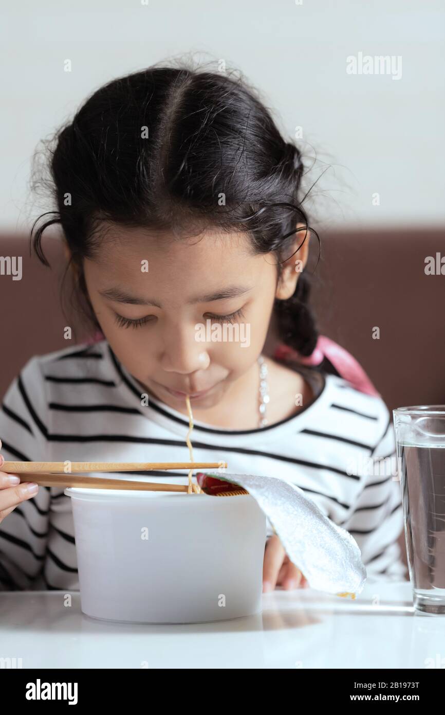 Little Asian girl sitting at white table to eating instant noodle select focus shallow depth of filed Stock Photo