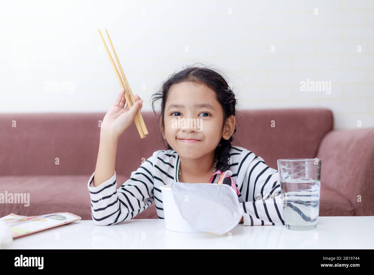 Little Asian girl sitting at white table to eating instant noodle and smile with happiness select focus shallow depth of filed Stock Photo