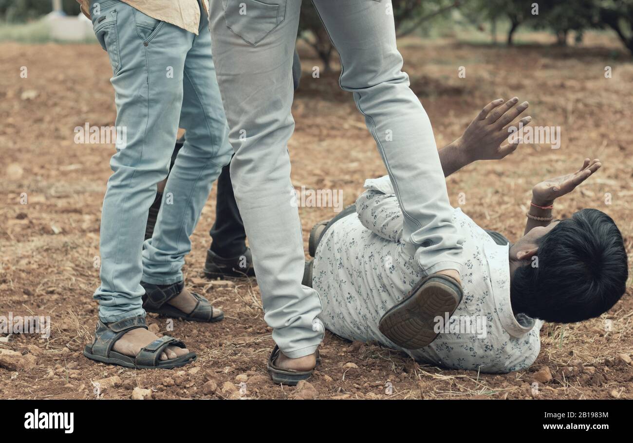 Concept of mob lynching - Group of people bullying, kicking a man - Close up of young adult males hitting a person on ground Stock Photo