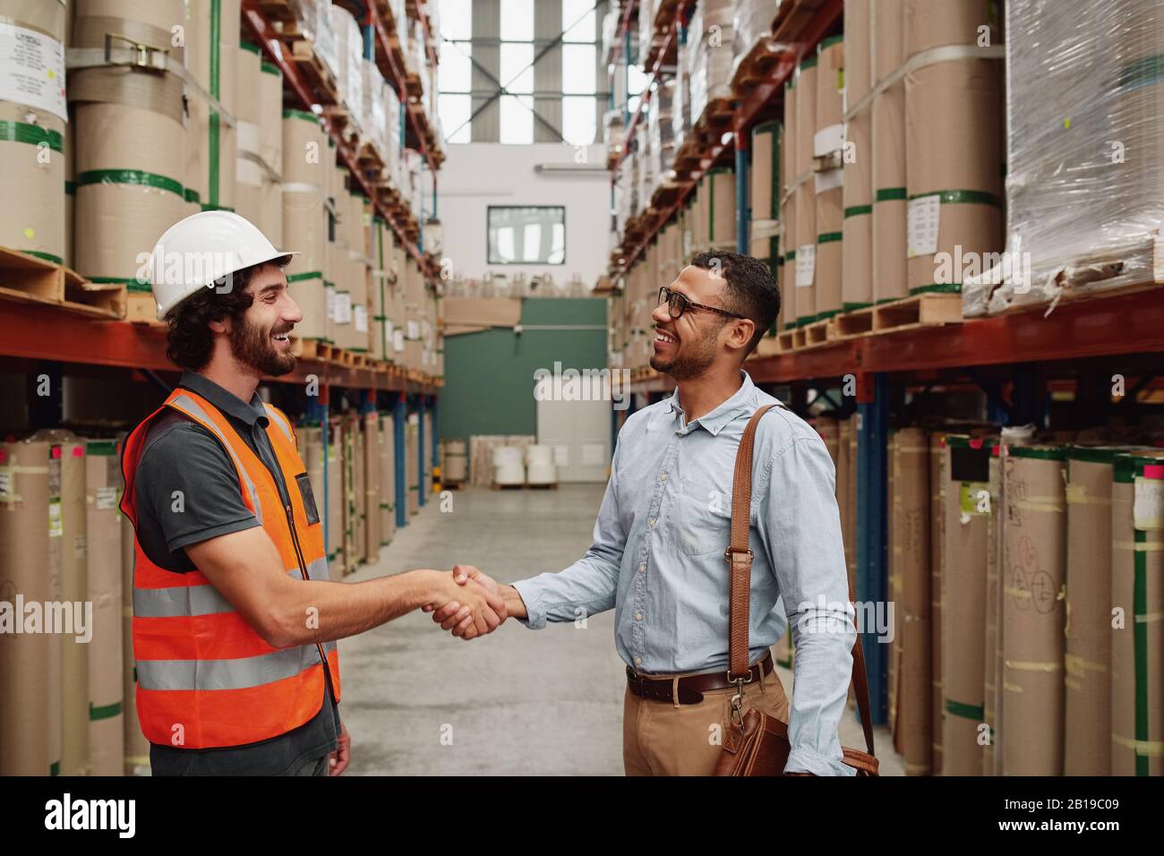 happy young business man in formal clothing making a deal with warehouse manager - two partners shaking hands on a new deal Stock Photo