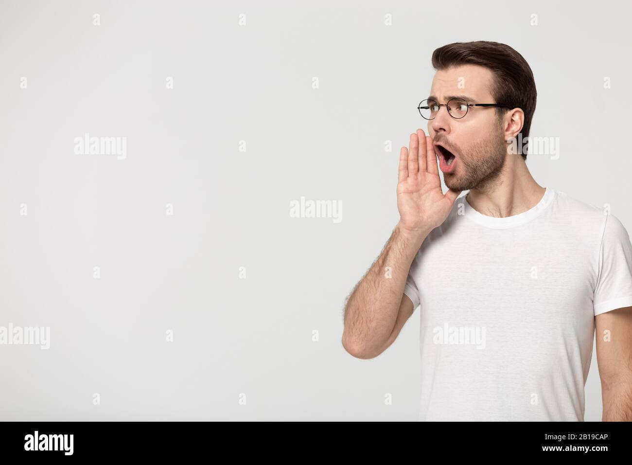 Millennial guy holding hand near mouth shouting, looking at copyspace. Stock Photo