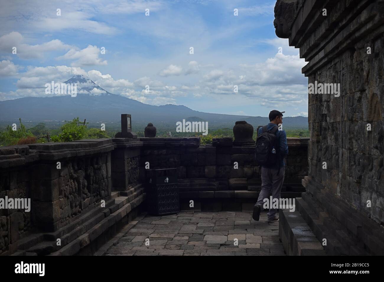Young man walks on Borobudur temple storey, with mountain view in the background. Stock Photo