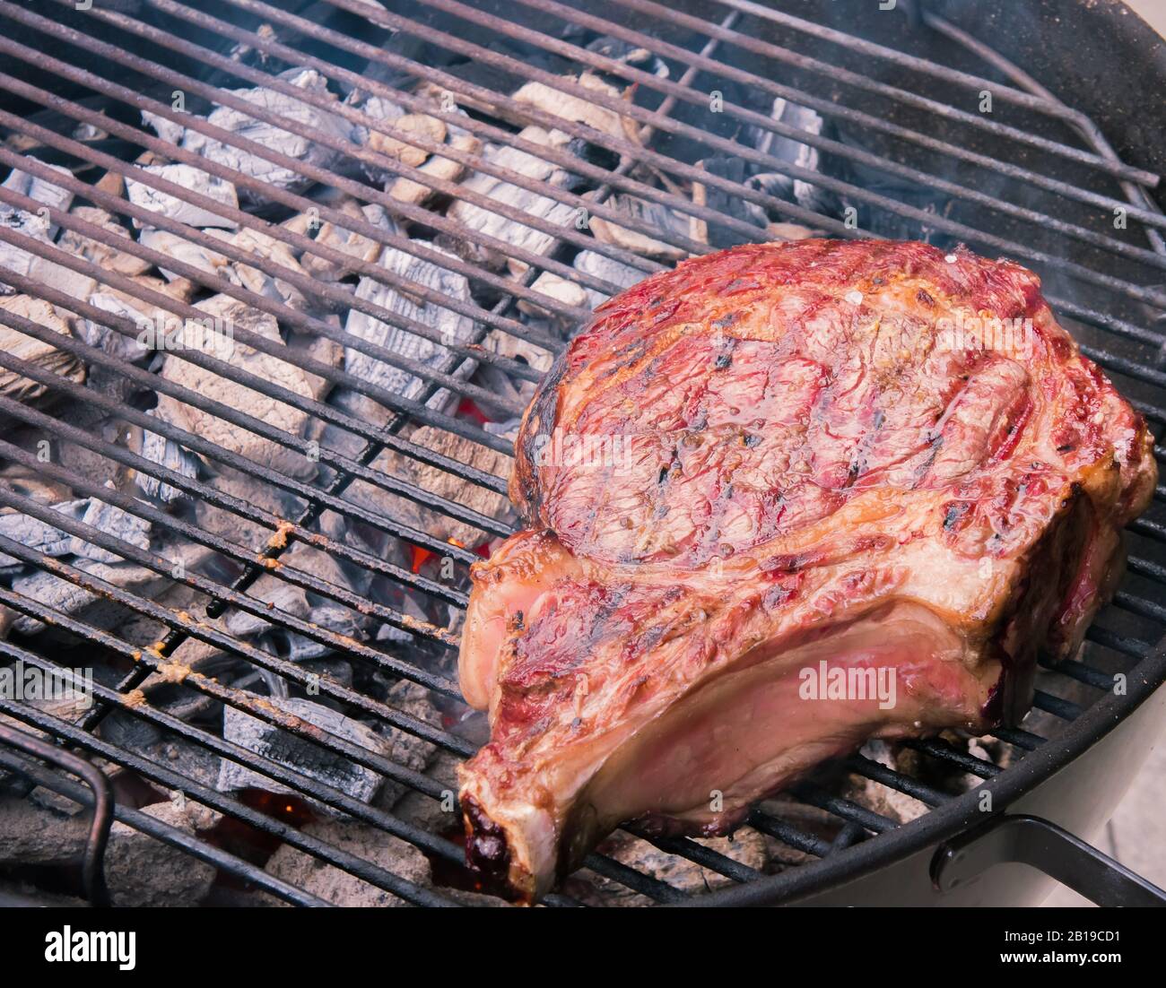 A juicy grilled piece of Tomahawk steak on a charcoal barbeque grill topped  with Himalyan salt Stock Photo - Alamy