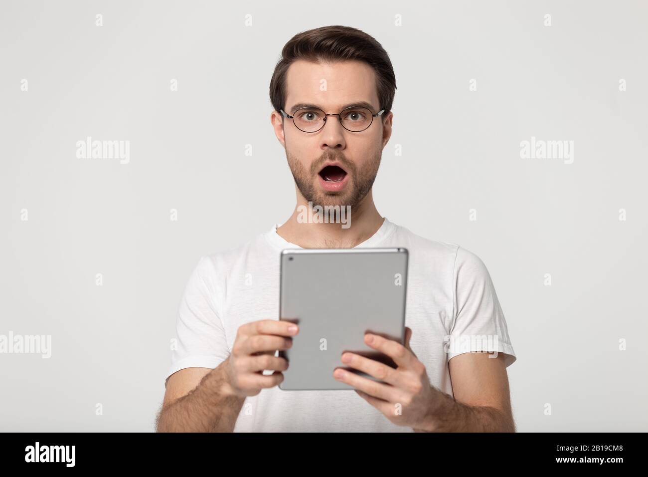 Surprised young man holding digital tablet, received unbelievable news. Stock Photo
