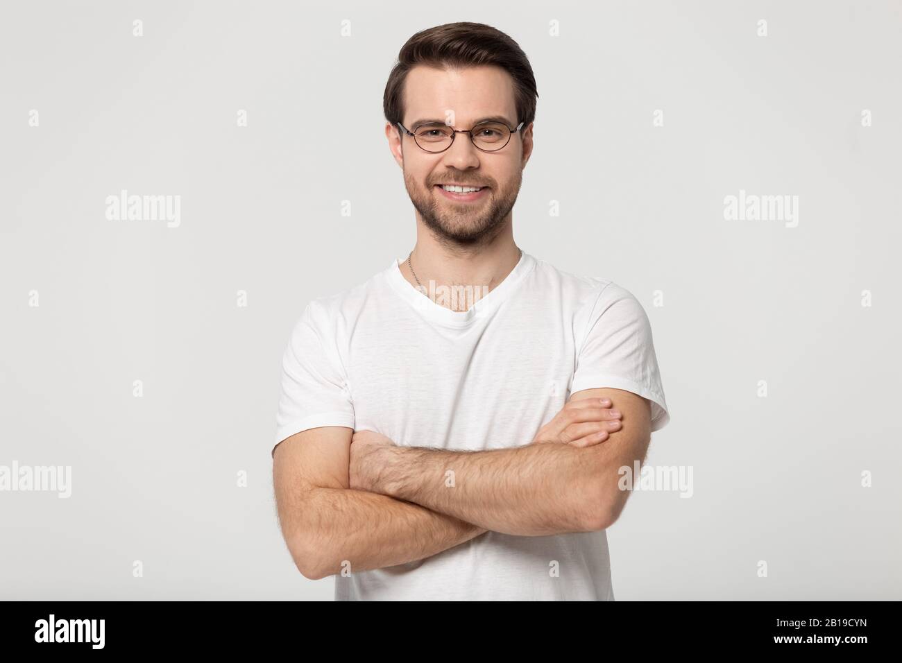 Happy millennial confident man in glasses standing with folded hands. Stock Photo