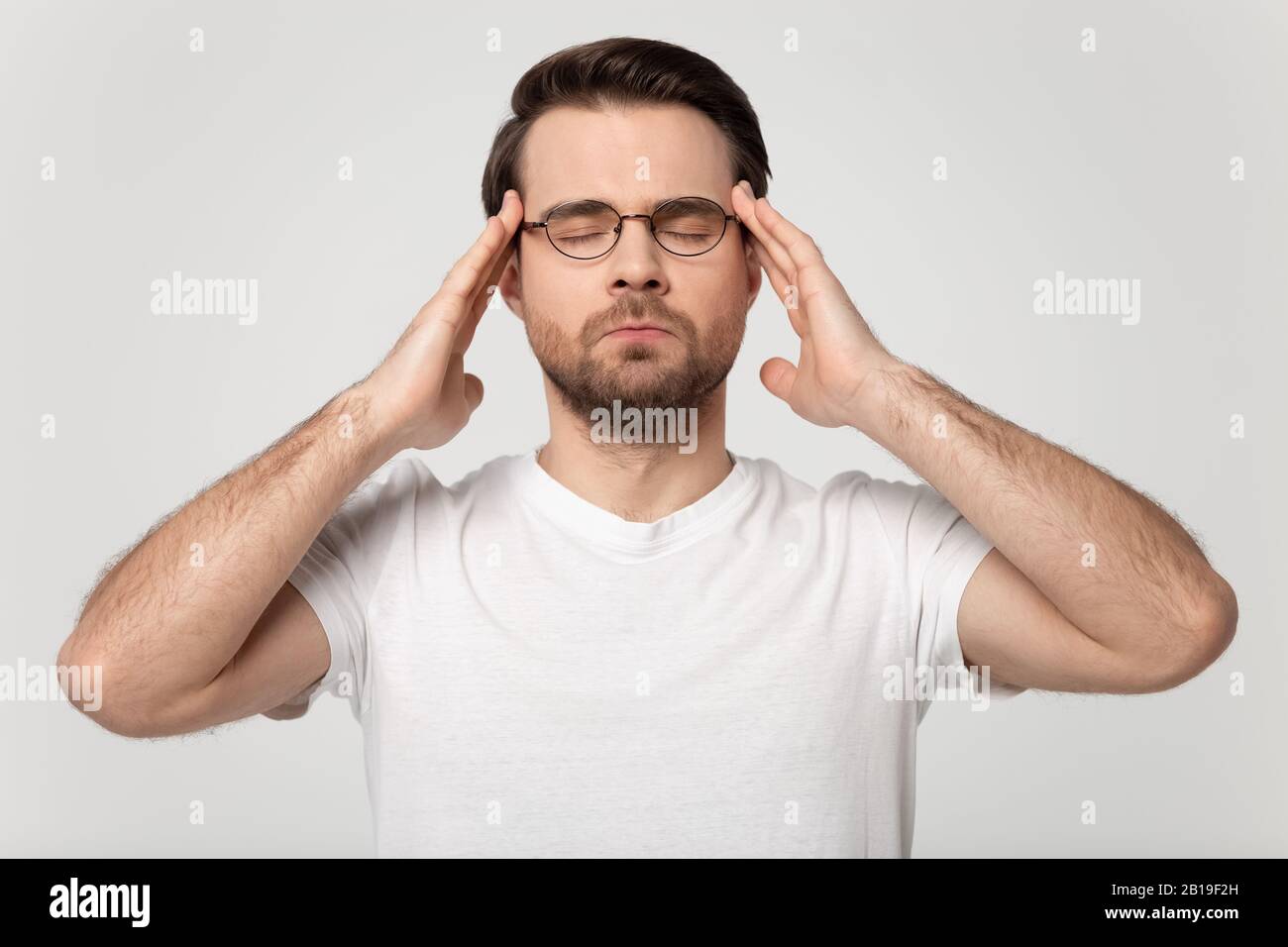 Stressed young guy in eyeglasses suffering from headache. Stock Photo