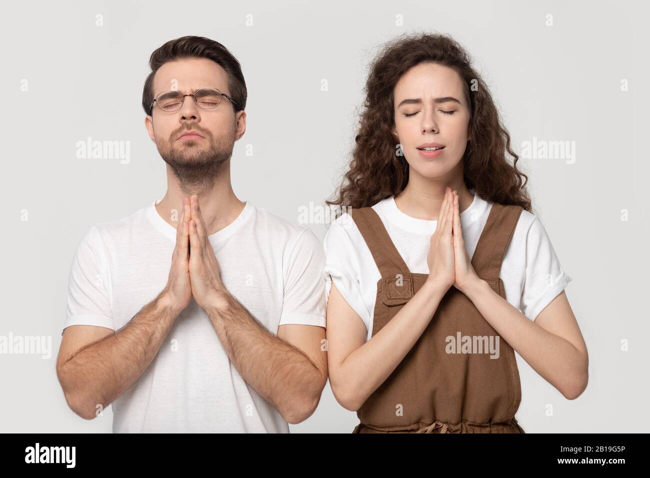 Hopeful couple standing with folded hands and closed eyes. Stock Photo