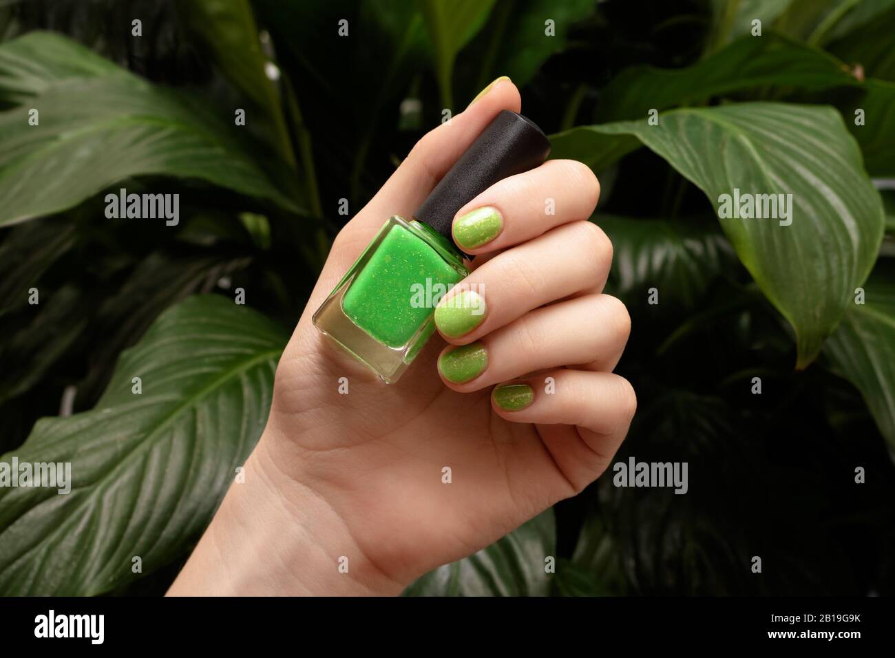 Female hand with green nail design holding nail polish bottle Stock Photo