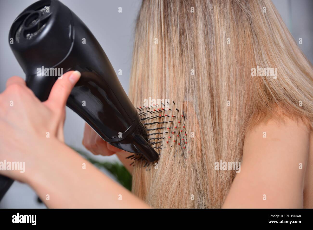 Woman with a hairdryer and comb brushing her wet blonde hair after