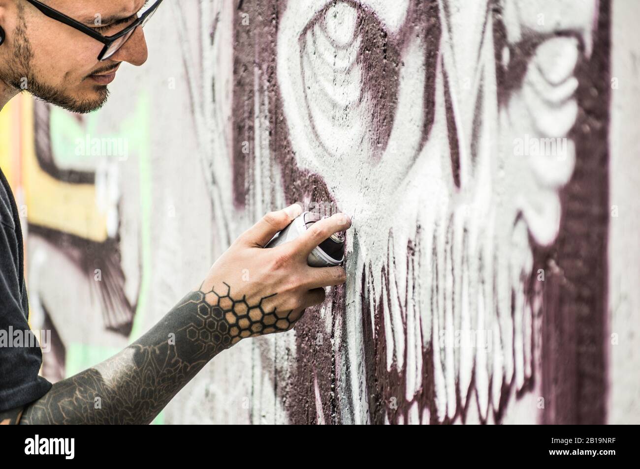 Tattoo graffiti writer painting with color spray his dark picture on the wall - Contemporary artist at work - Urban lifestyle,street art concept - Foc Stock Photo