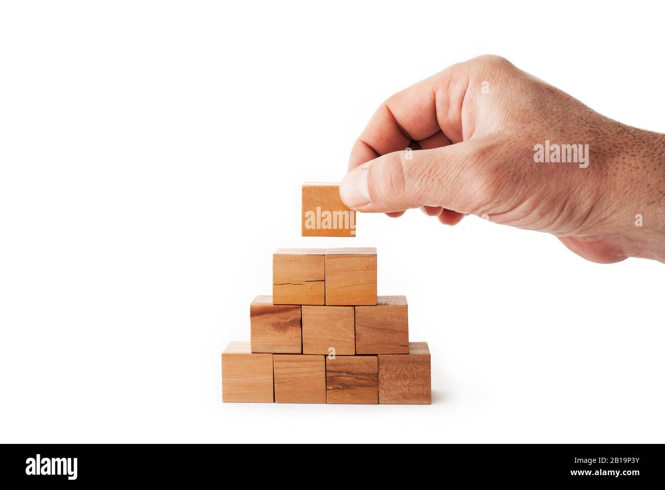 A hand is putting the last cube for building a pyramid with wooden cubes on white background. Success, strategy, improvement and victory concept Stock Photo