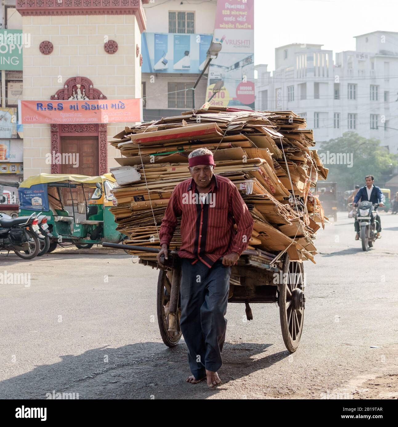 Jamnagar, Gujarat/India - December 18 2018: A man pulls a cart full of cardboard scrap while walking barefoot in the sun on the streets of Jamnagar. Stock Photo