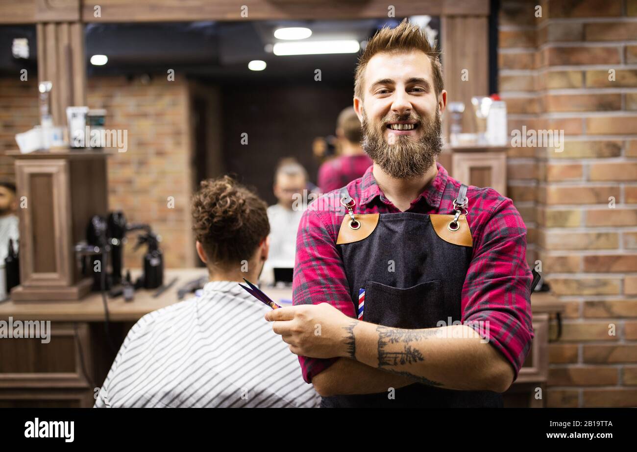 Portrait of happy young barber with client at barbershop and smiling. Stock Photo