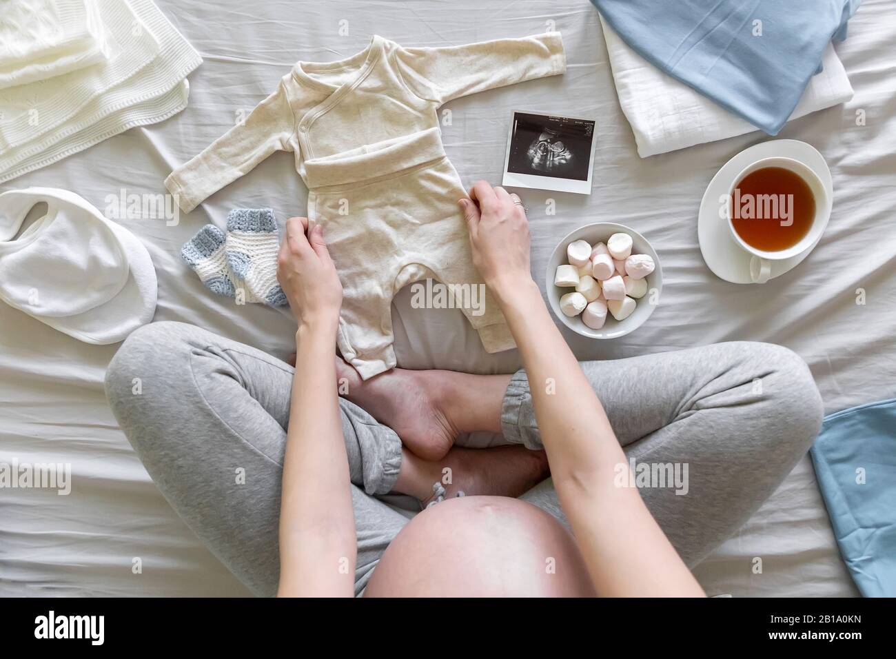 Top view of pregnant woman in the bed preparing clothes for baby boy, pregnancy and birth concept Stock Photo